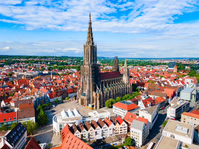 Luftaufnahme des Ulmer Münsters mit seinem markanten Kirchturm, umgeben von roten Dächern der Altstadt.