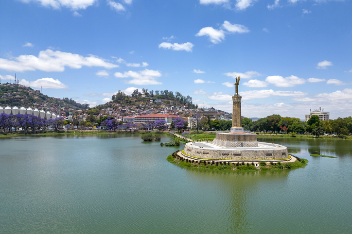 Ein Denkmal auf einer kleinen Insel in einem See in Antananarivo, umgeben von Wasser und Stadtblick.