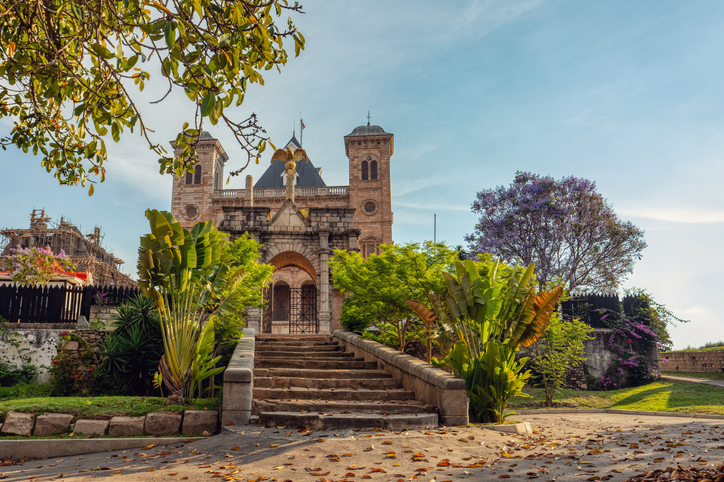 Ein historisches Bauwerk mit Treppe, tropischen Pflanzen und blühenden Bäumen in Antananarivo.