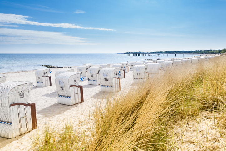Weiße Strandkörbe am Sandstrand von Timmendorfer Strand mit Dünengras und Blick aufs Meer.