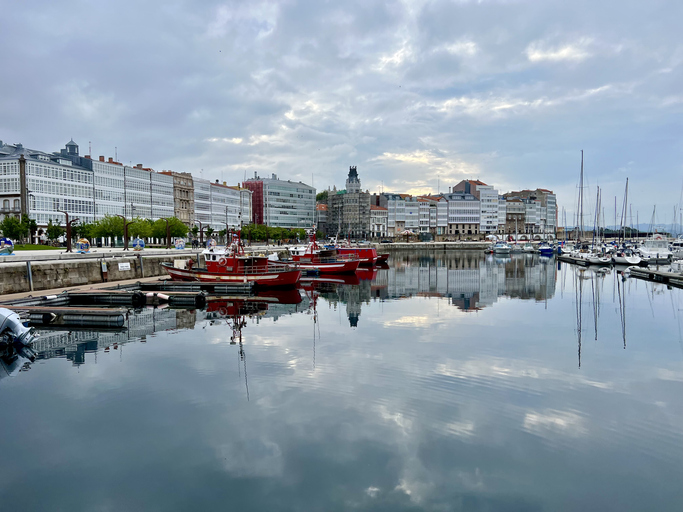 Yachthafen und Uferpromenade in A Coruña mit spiegelglattem Wasser und bewölktem Himmel