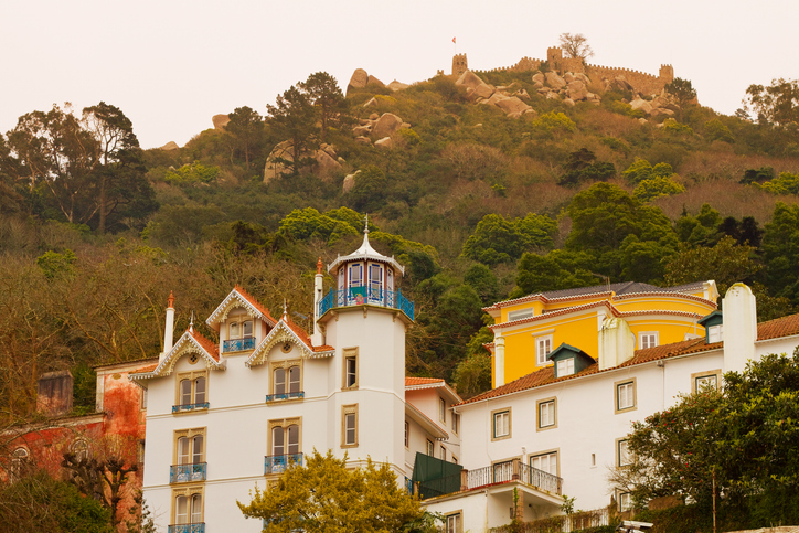 Bunte Häuser stehen am Hang von Sintra, darüber verläuft die Mauer einer alten Festung.