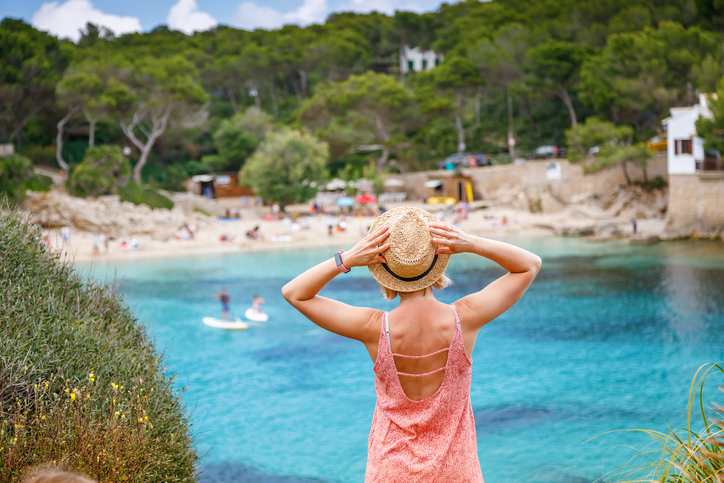 Frau blickt auf die türkisfarbene Bucht und den Strand von Cala Gat