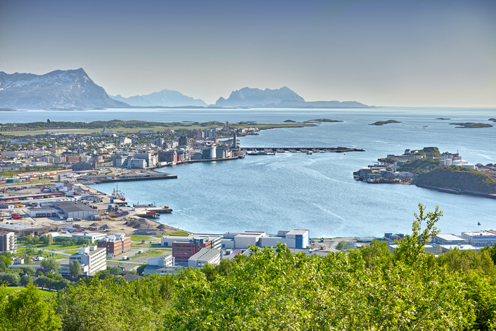 Blick über eine norwegische Hafenstadt mit Meer, Industrieanlagen und Bergkulisse im Hintergrund.