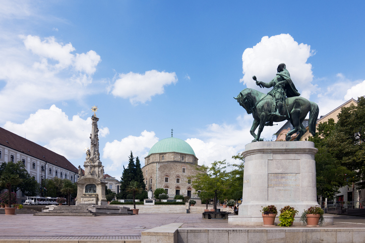 Historischer Platz in Pécs mit Reiterstatue, Denkmal und Gebäude mit grüner Kuppel.