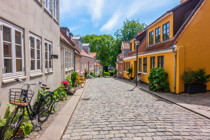Fahrräder stehen an einer gepflasterten Straße mit bunten Häusern in der Altstadt von Odense.
