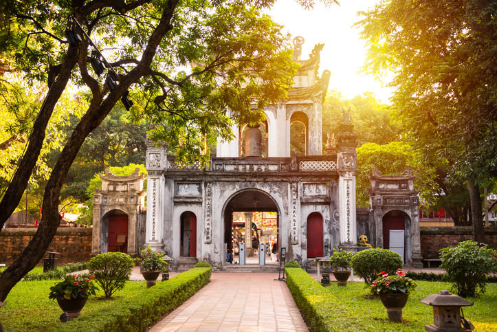 Ein altes steinernes Tor steht in einer gepflegten Gartenanlage mit Bäumen und Wegen in Hanoi.