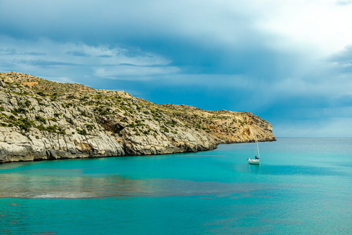 Ein Segelboot liegt vor der türkisfarbenen Küste von Cala Sant Vicenç unter dramatischem Himmel