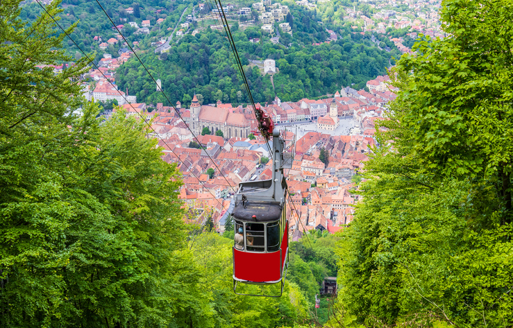 Rote Seilbahnkabine über den Wäldern mit Blick auf die Altstadt von Brașov