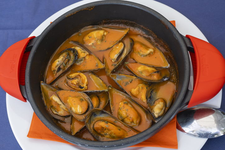 Ein Topf mit Miesmuscheln in würziger Sauce steht servierfertig auf einem Tisch.