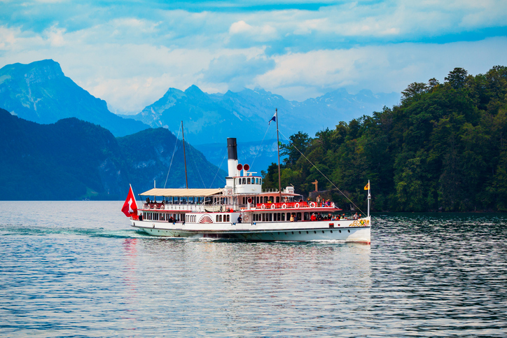 Ein historisches Dampfschiff fährt auf dem Vierwaldstättersee vor Bergen und grünen Ufern.