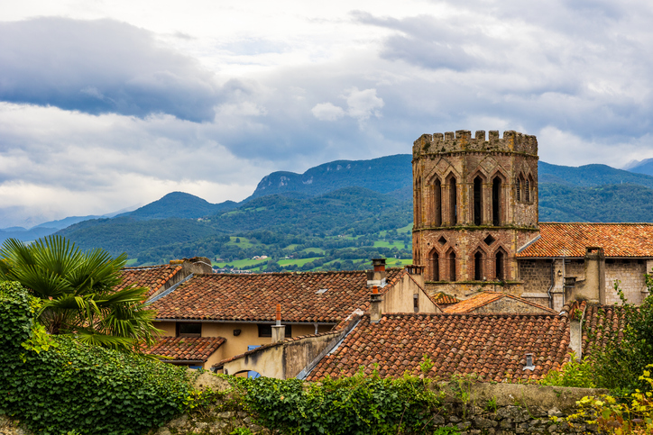 Alter steinerner Kirchturm ragt über die roten Dächer von Saint-Girons vor bewaldeten Hügeln