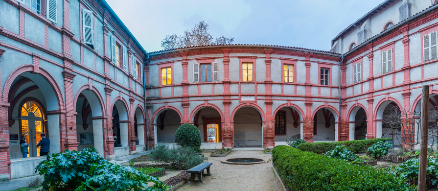 Historischer Innenhof mit roten Backsteinarkaden und Garten im Musée Ingres Bourdelle in Montauban.