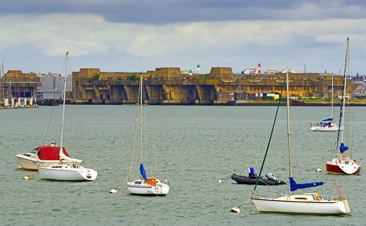 Segelboote auf dem Wasser mit großer Bunkeranlage im Hintergrund in Lorient