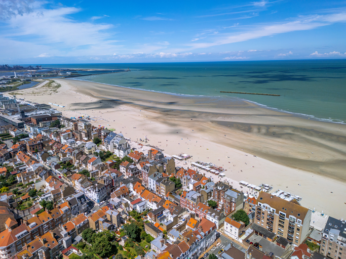 Luftaufnahme eines breiten Sandstrands mit Stadtbebauung an der Küste von Dunkerque.