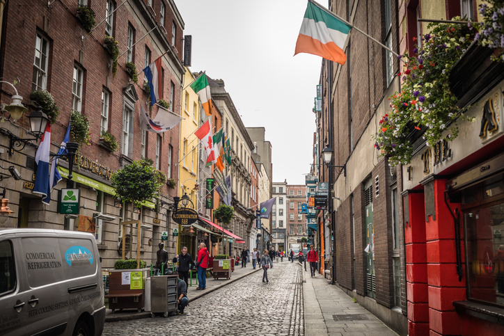 Eine schmale Straße in Dublin ist mit mehreren irischen Flaggen geschmückt und von alten Gebäuden gesäumt.