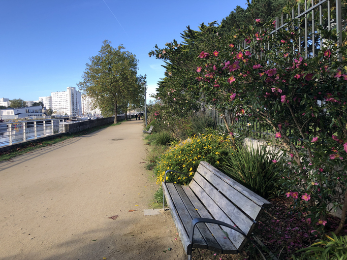 Parkbank an einem Weg mit Blumen und Büschen nahe dem Wasser in Lorient