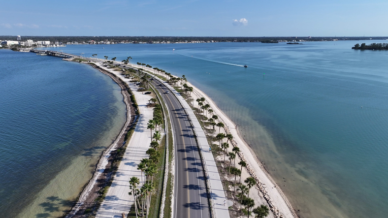 Eine lange Straße führt zwischen Wasserflächen und Palmen durch die Tampa Bay.