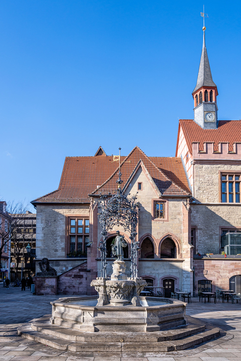Der Gänseliesel-Brunnen steht vor dem Alten Rathaus in Göttingen unter blauem Himmel.