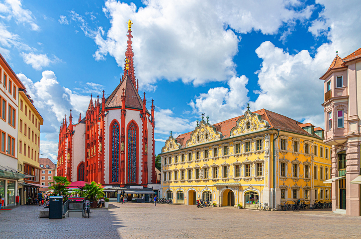Die rote Marienkapelle und das gelbe Falkenhaus am Marktplatz in Würzburg unter blauem Himmel.