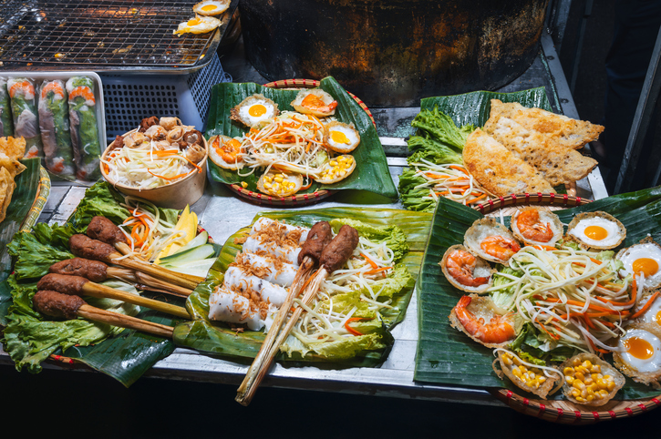 Verschiedene vietnamesische Speisen liegen auf grünen Blättern an einem Streetfood-Stand in Hanoi.