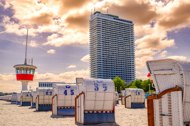 Strandkörbe und Rettungsturm am Strand von Timmendorfer Strand mit Hochhaus im Hintergrund.