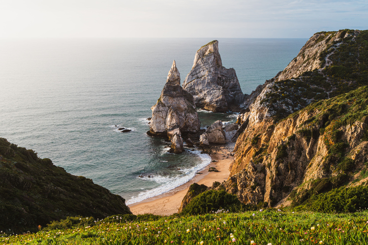 Hohe Felsen ragen an der Küste bei Sintra über einen kleinen Sandstrand ins Meer.
