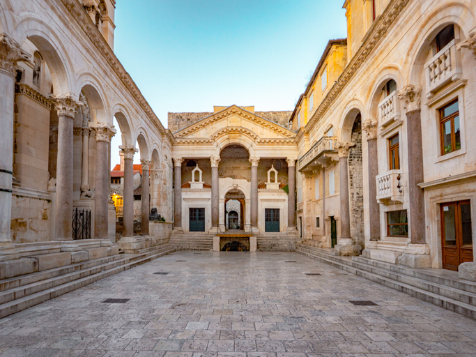 Ein historischer Innenhof mit Säulen, Steinbögen und hellen Fassaden im Diokletianpalast von Split.