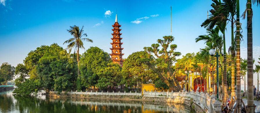 Eine Pagode am Wasser in Hanoi, umgeben von Bäumen und warmem Abendlicht.