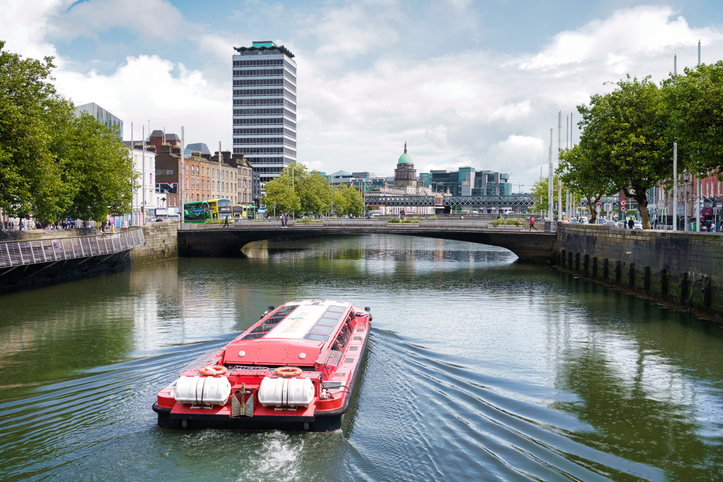 Ein rotes Ausflugsboot fährt auf dem River Liffey durch das Zentrum von Dublin unter einer Brücke hindurch.
