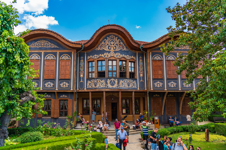 Historisches, reich verziertes Haus in Plowdiw mit dunkler Fassade, Holzelementen und kleinem Garten davor.