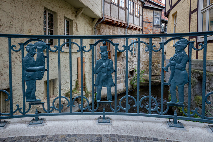 Ein Geländer mit Figurenmotiven steht an einem Wasserlauf zwischen historischen Häusern in Quedlinburg.