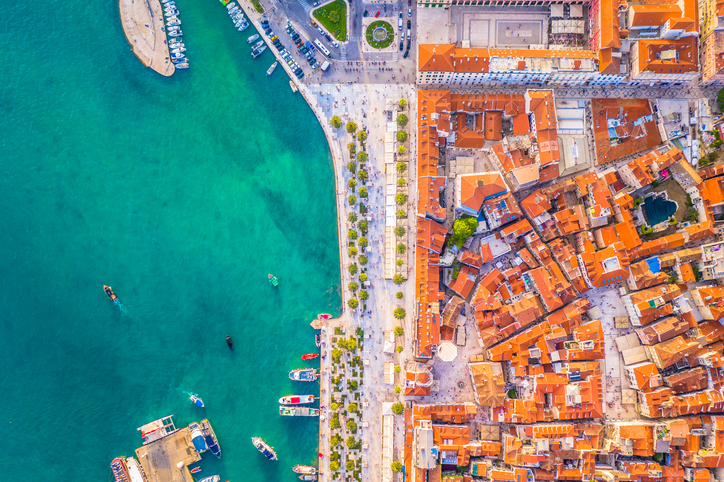 Luftaufnahme von Split mit türkisblauem Wasser, Hafenpromenade und roten Dächern der Altstadt.