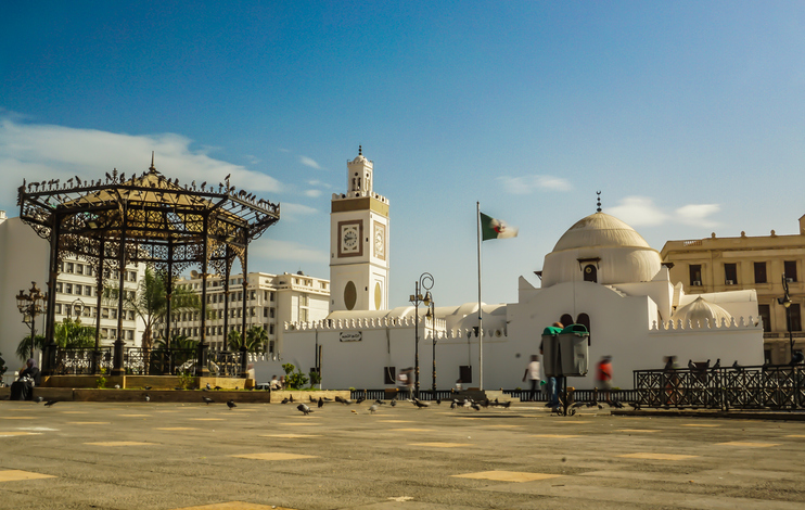Eine weiße Moschee mit Minarett und Kuppel steht an einem weiten Platz im Zentrum von Algier.