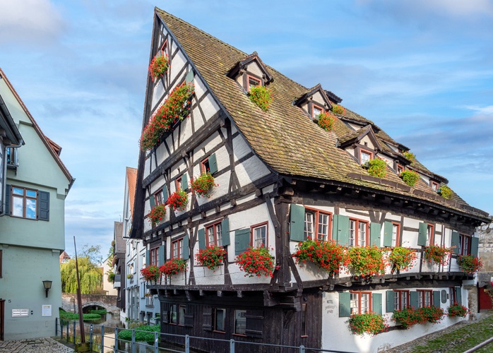 Großes Fachwerkhaus mit vielen roten Blumenkästen an Fenstern in einer historischen Gasse in Ulm.