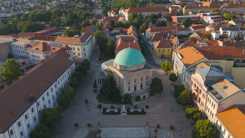 Luftaufnahme von Pécs mit Gebäude mit grüner Kuppel, roten Dächern und historischem Stadtzentrum.