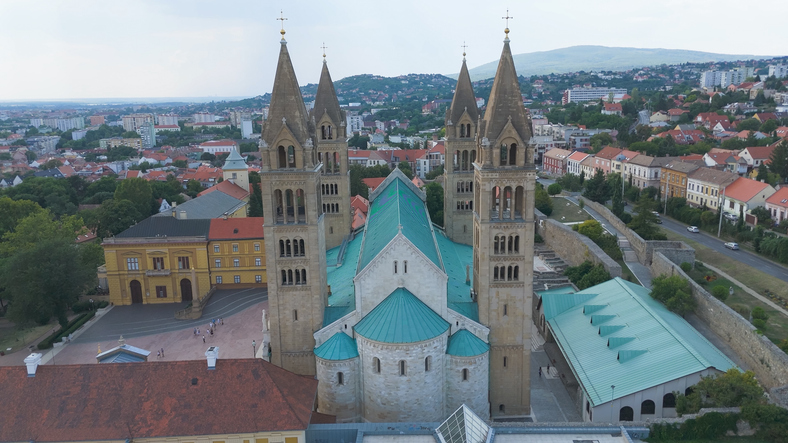 Luftaufnahme der Kathedrale von Pécs mit vier Türmen, grünen Dächern und umliegender Stadtlandschaft.