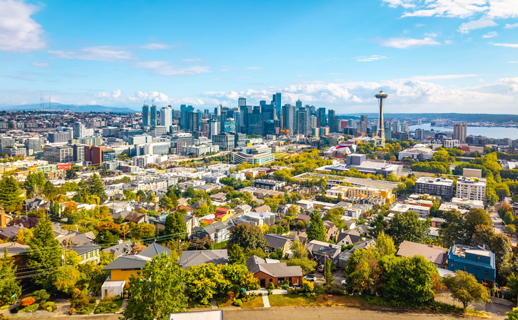 Blick über Seattle mit Space Needle, Hochhäusern, Wohnvierteln und Wasser im Hintergrund.