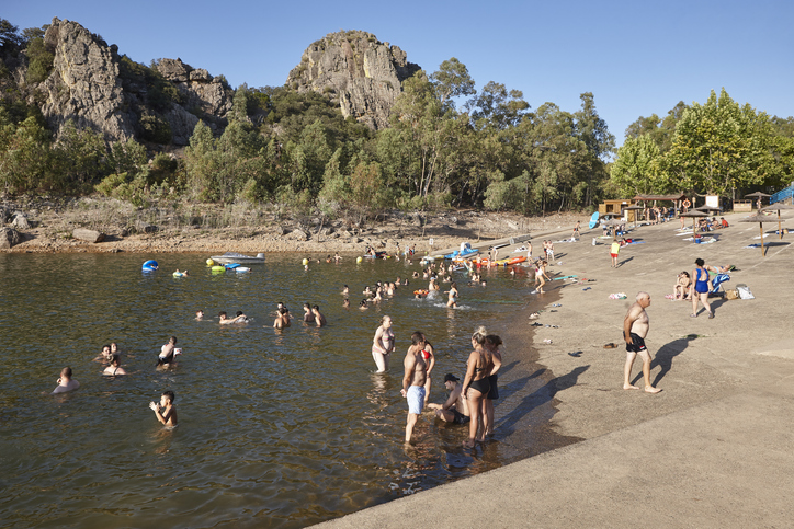 Menschen baden an einem Seeufer mit Felsen und Bäumen in der Umgebung von Badajoz