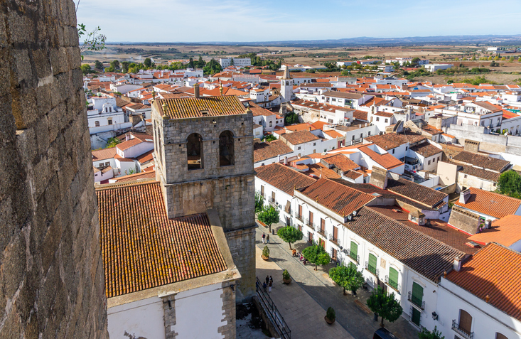 Blick von oben auf einen Kirchturm, helle Häuser und Straßen in einer Stadt nahe Badajoz