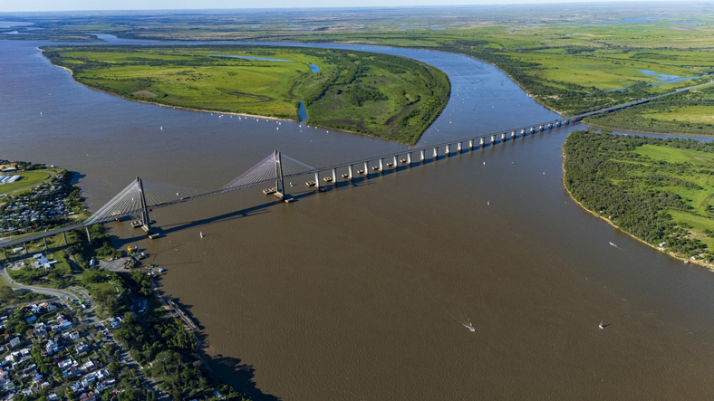 Eine lange Brücke führt über den breiten Paraná-Fluss zwischen grünen Uferlandschaften.