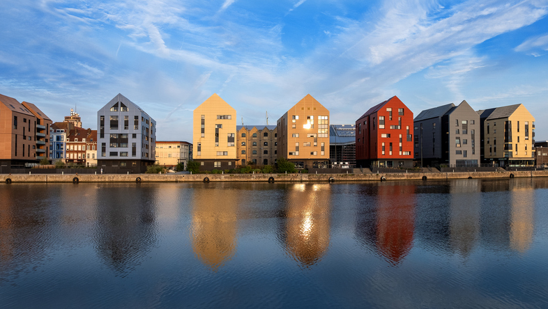 Bunte moderne Häuser spiegeln sich am Wasser in einem Hafenviertel von Dunkerque.