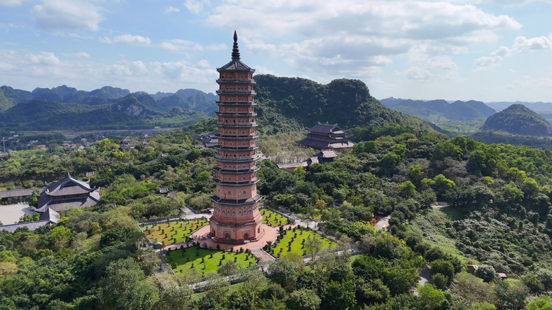 Eine hohe Pagode steht inmitten einer grünen Landschaft mit Bergen im Hintergrund in Nordvietnam.