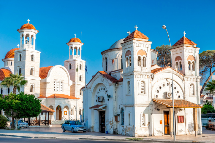 Helle orthodoxe Kirche mit roten Kuppeln und Türmen unter blauem Himmel in Larnaka
