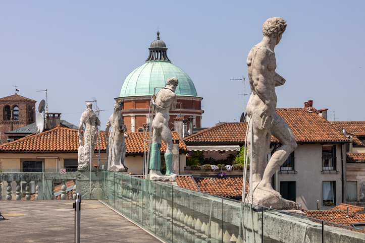Statuen stehen auf einer Terrasse über den roten Dächern von Vicenza mit Kuppel im Hintergrund.