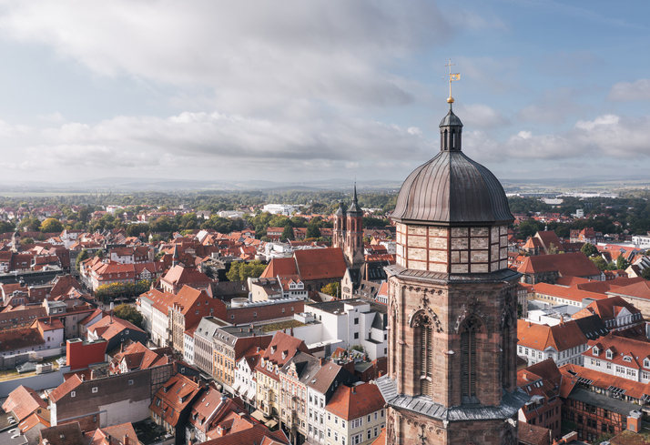 Luftaufnahme von Göttingen mit einem Kirchturm im Vordergrund und roten Dächern der Altstadt.