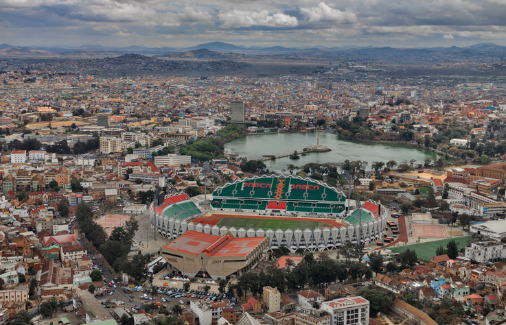 Luftaufnahme von Antananarivo mit einem großen Stadion, einem See und dicht bebauter Stadtlandschaft.
