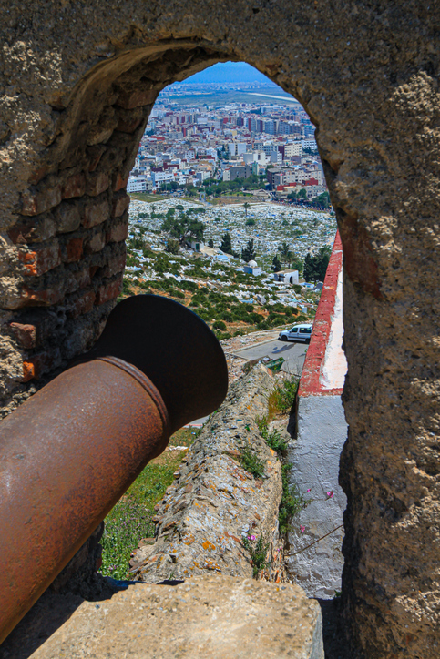 Blick durch eine steinerne Öffnung mit alter Kanone auf die Stadt Tetouan