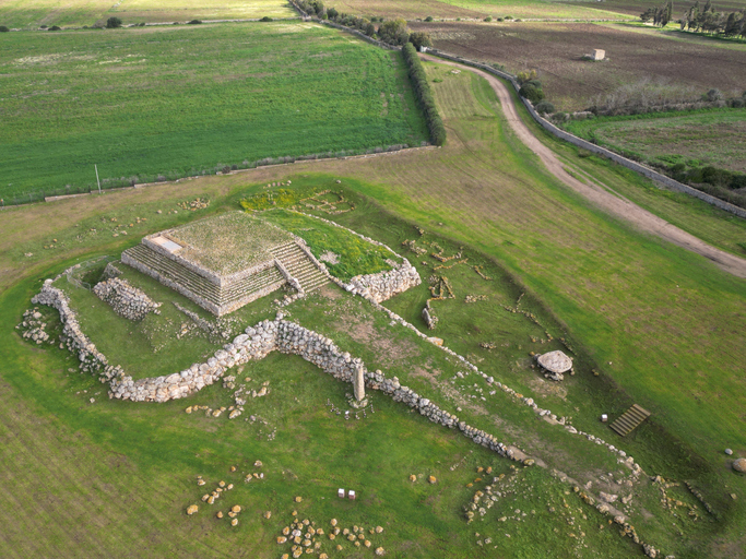 Luftaufnahme einer archäologischen Anlage mit steinernen Mauern und gestufter Plattform im Umland von Sassari