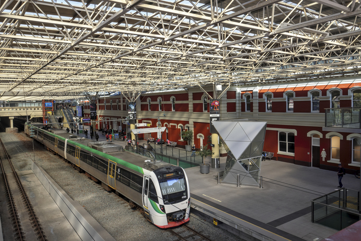 Moderner Bahnhof in Perth mit Zug, überdachten Gleisen und Reisenden auf dem Bahnsteig.